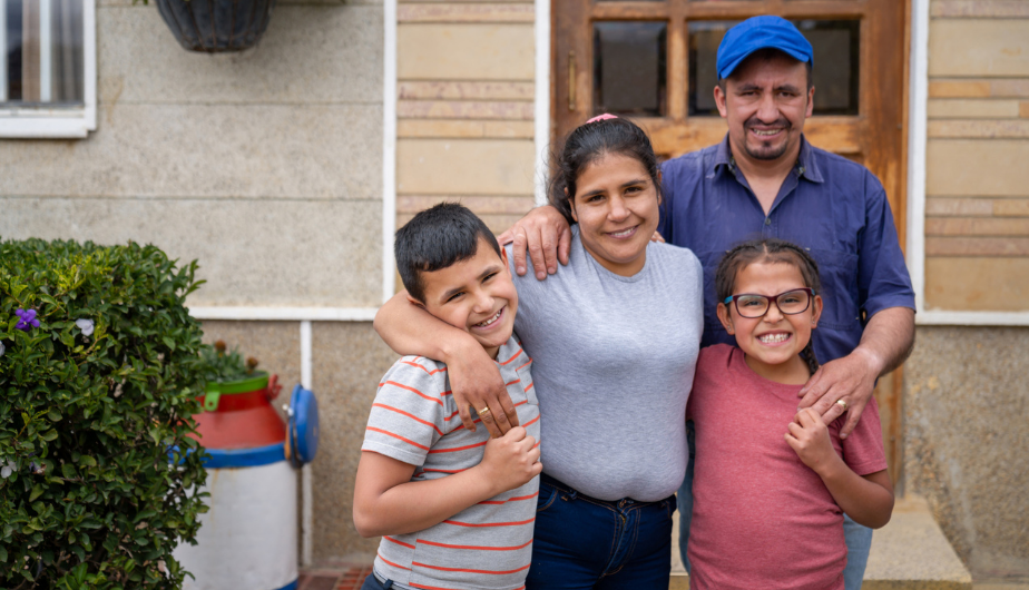 Family smiling in front of house