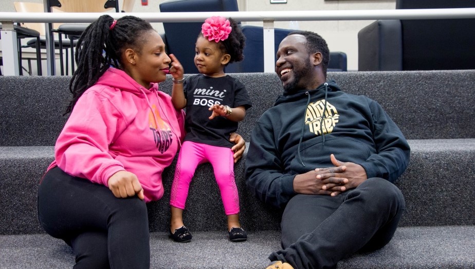 A young Black family sit on some stairs