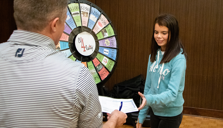 young woman besides game wheel accepts paper and pen