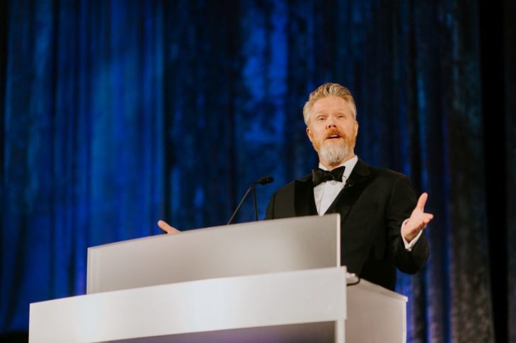 bearded well dressed man presenting at podium