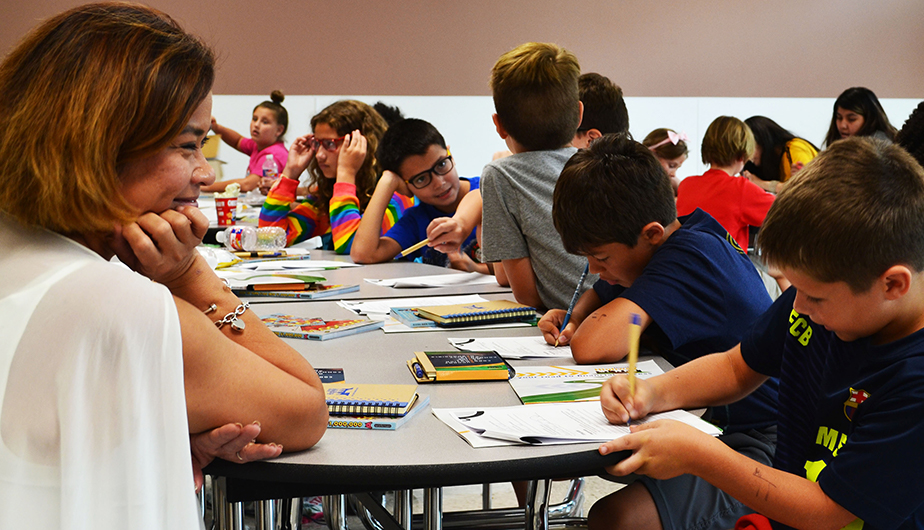 group of children gathered around table at school with teacher