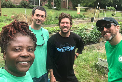 4 smiling people on a team near a garden plot