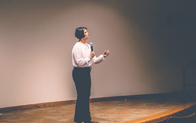 woman in spotlight speaking on stage