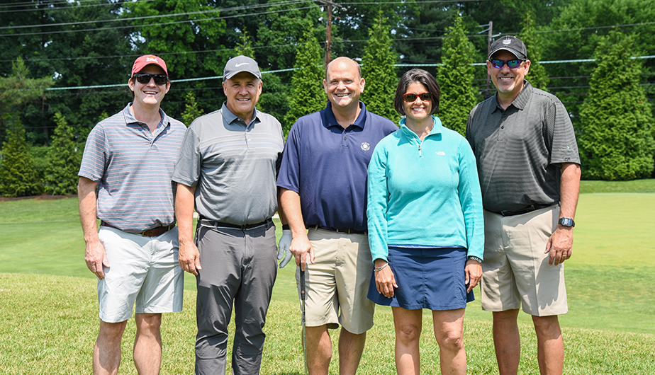 4 men and 1 woman standing on golf green smiling